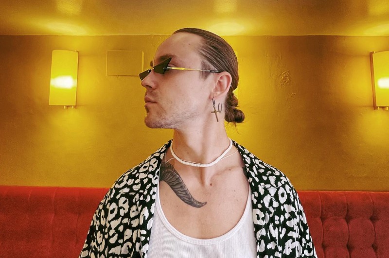 Артем Пивоваров у яскравому вбранні та вузьких сонцезахисних окулярах, із татуюванням на шиї та модною зачіскою.