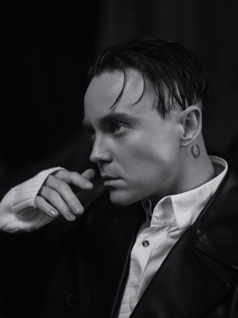 Чорно-біле фото Артема Пивоварова у шкіряному піджаку з поглядом убік та татуюванням на шиї.