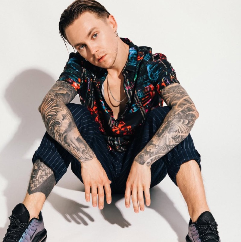 Артем Пивоваров сидить на підлозі в яскравій сорочці з татуюваннями на руках і ногах.